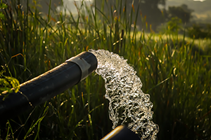 An outdoor pipe with a large stream of water flowing out of it onto a field with tall grass.