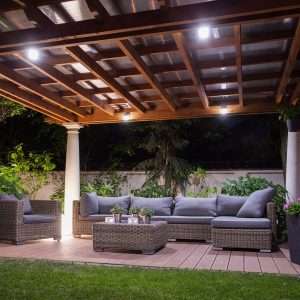 Landscape and overhead lighting under a pergola outdoor living space at night.